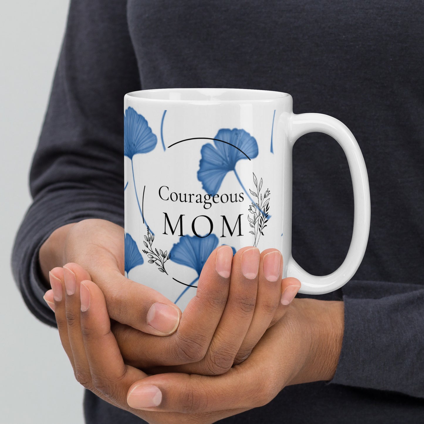 Person holding a mug with 'Courageous Mom' text and blue floral design.