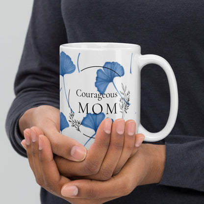 Person holding a mug with 'Courageous Mom' text and blue floral design.